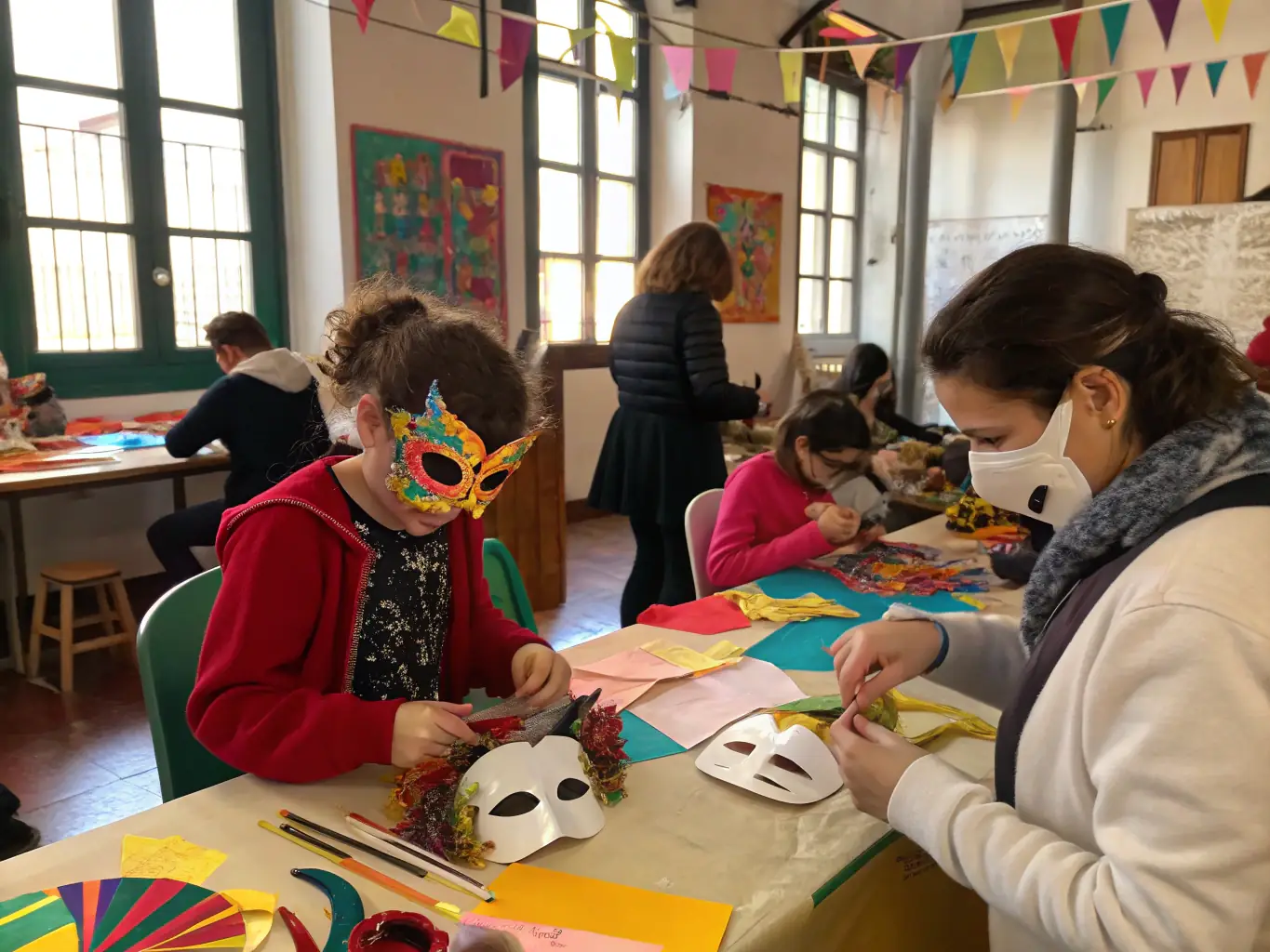 A vibrant image depicting participants in a costume-making workshop, focused on Venetian-style masks, with various tools and materials scattered around the tables, showcasing hands-on learning and creative collaboration.